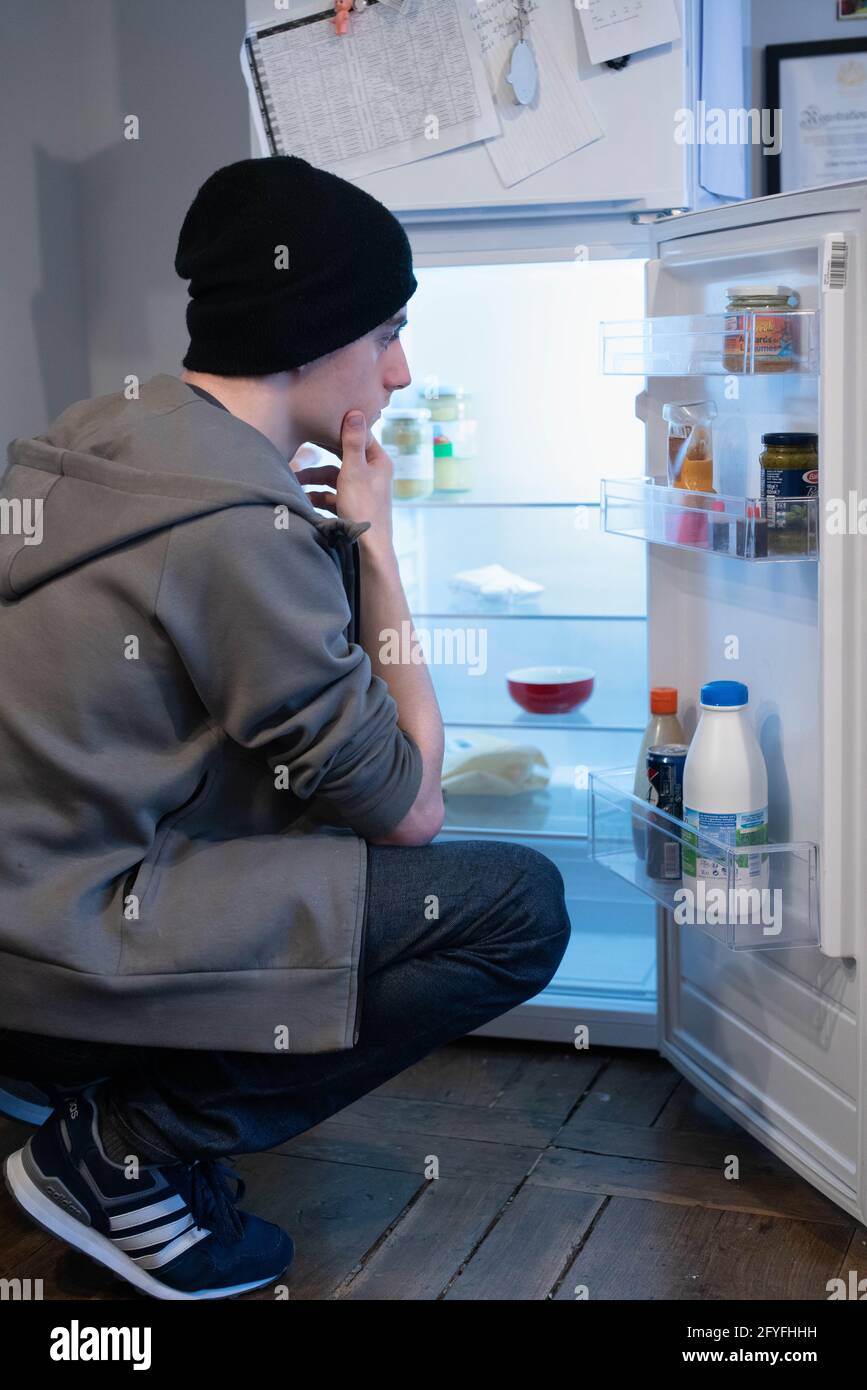 Jeune homme devant son réfrigérateur. Illustration de la précarité des jeunes, France. Banque D'Images