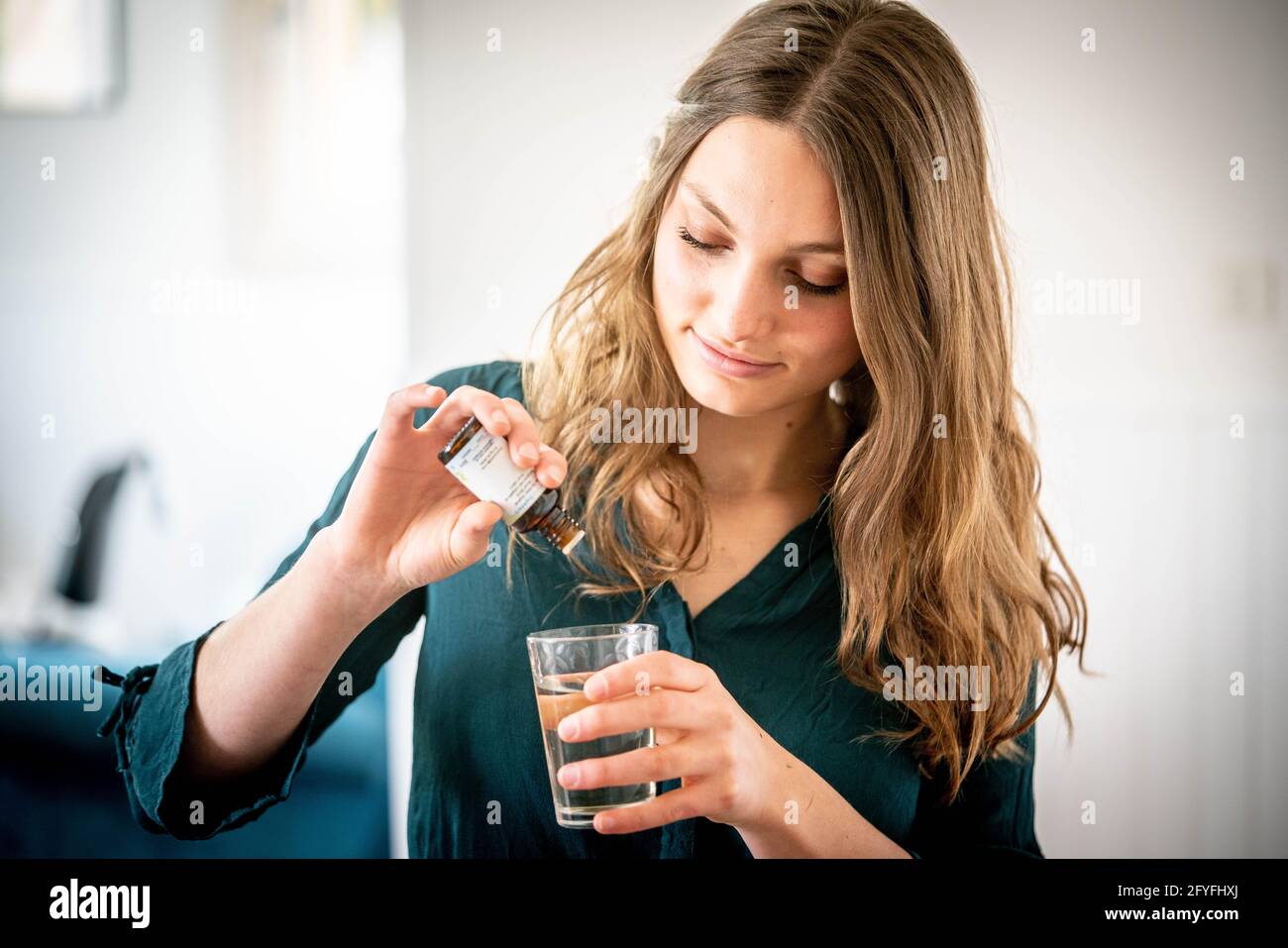 Femme versant des gouttes de macérate dans un verre d'eau. Banque D'Images