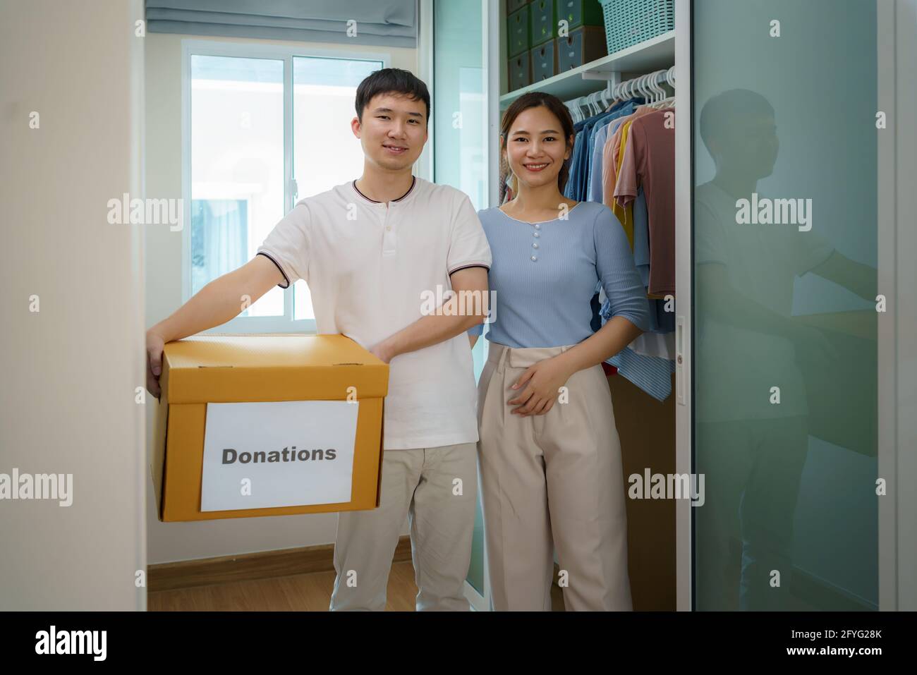 Les couples asiatiques sont debout près du placard des vêtements dans le dressing portant une boîte de vêtements donnés à apporter au centre de dons. Banque D'Images