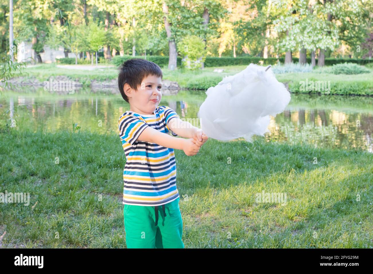 Un enfant de 4 ans dans un t-shirt rayé mange des bonbons de coton sur un bâton dans la nature avec un emplacement pour la copie de texte. Bonne enfance et enfants Banque D'Images