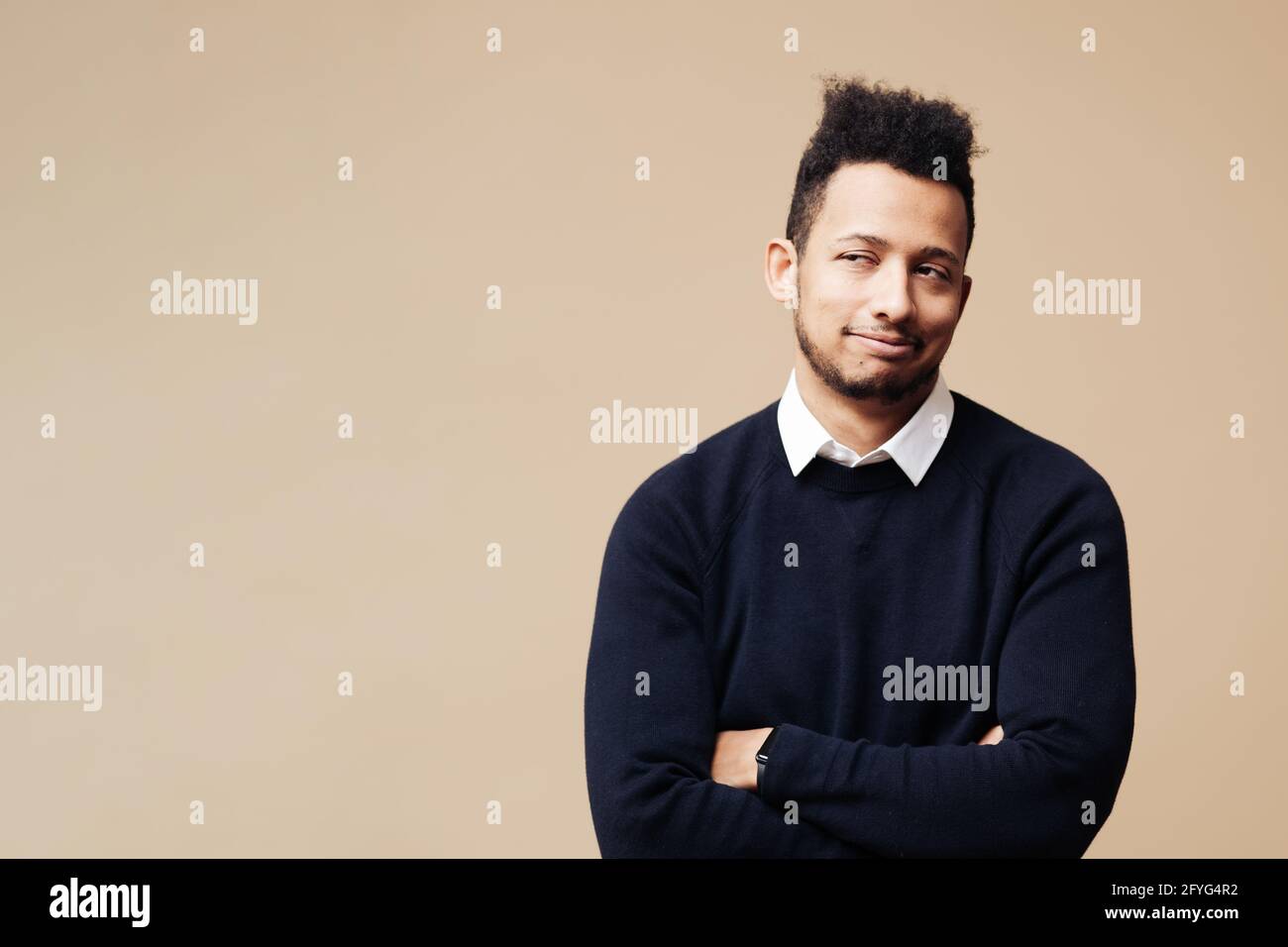 Homme afro aux mains croisées et au sourire mystérieux cherchant à copier l'espace sur fond beige. Les hommes ont une idée brillante Banque D'Images