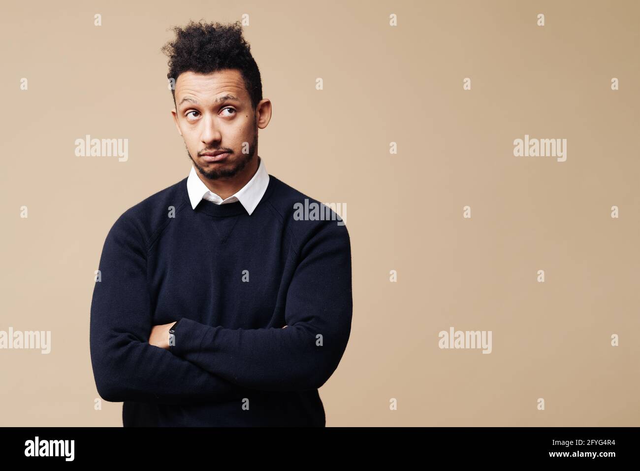 Photo courte d'un jeune Afro attentionné debout à bras croisés sur fond beige avec espace de copie Banque D'Images