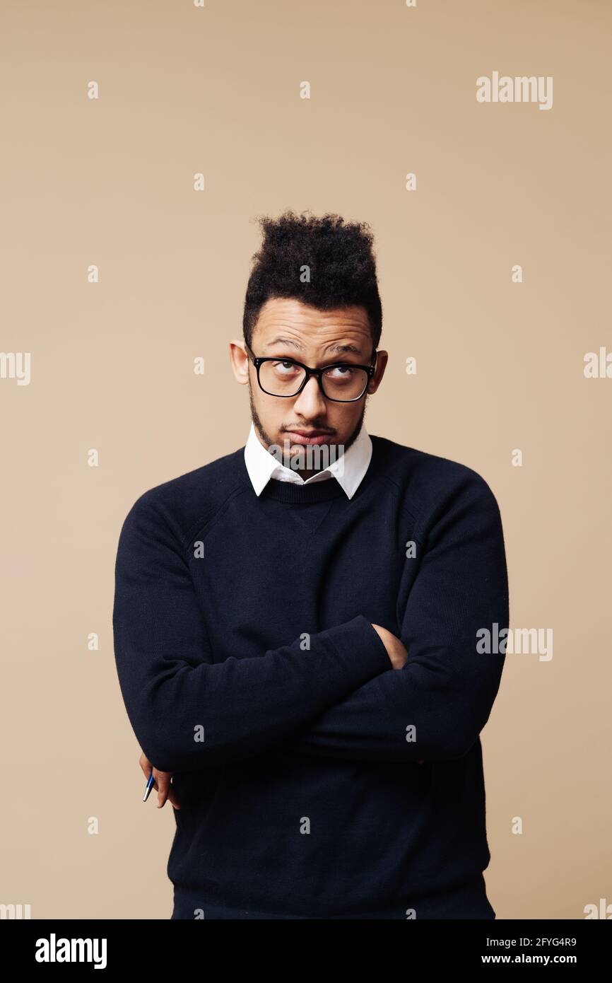 Photo courte d'un jeune Afro attentionné debout à bras croisés sur fond beige Banque D'Images