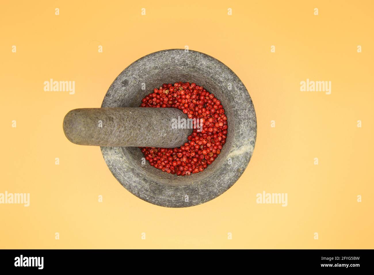 Vue de dessus gros plan sur mortier en pierre de basalte gris isolé avec pilon et cornes de poivron rouge, fond blanc jaune (point central) Banque D'Images