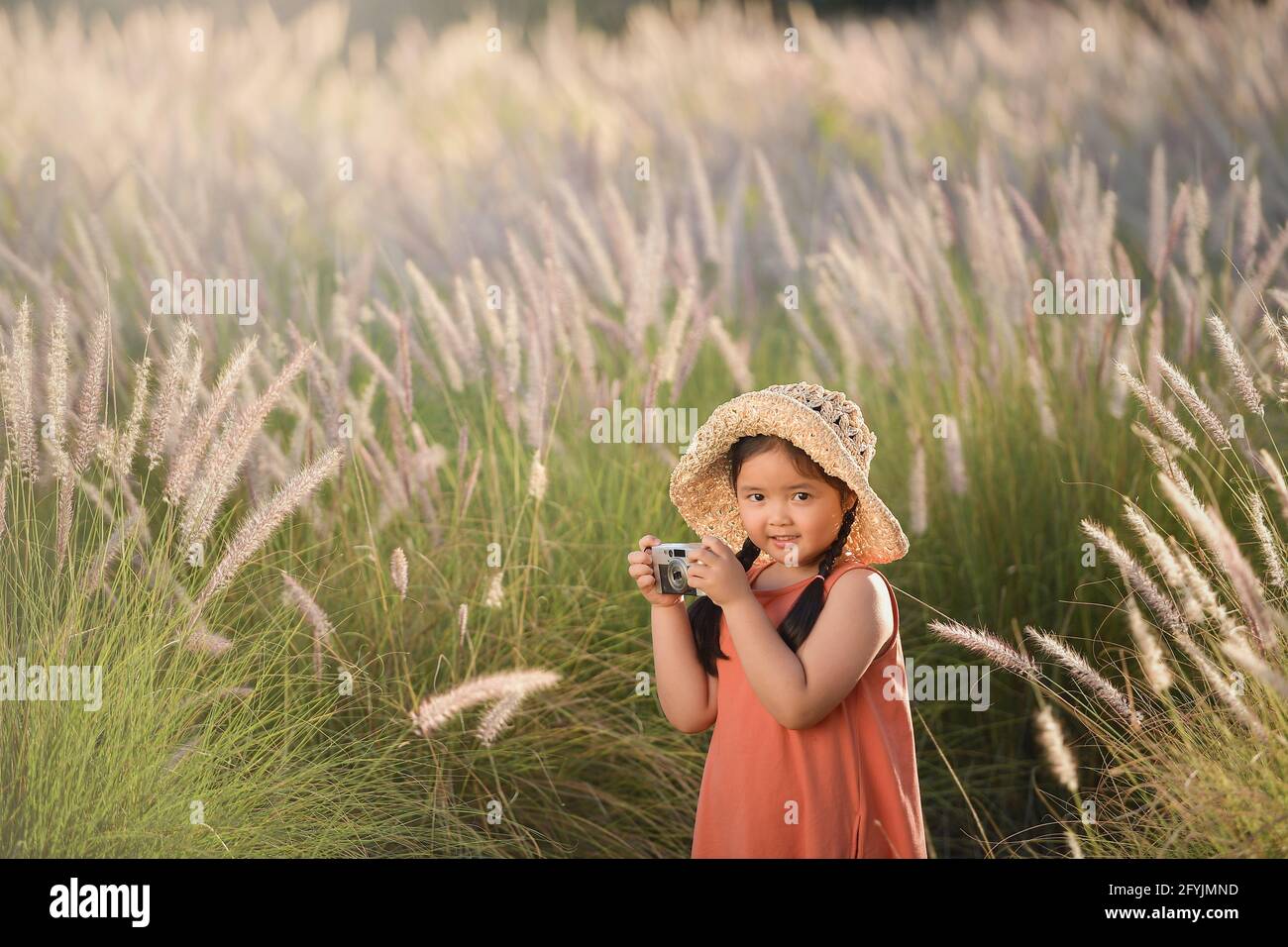 Fille souriante debout au milieu de l'herbe longue prenant une photo, Thaïlande Banque D'Images