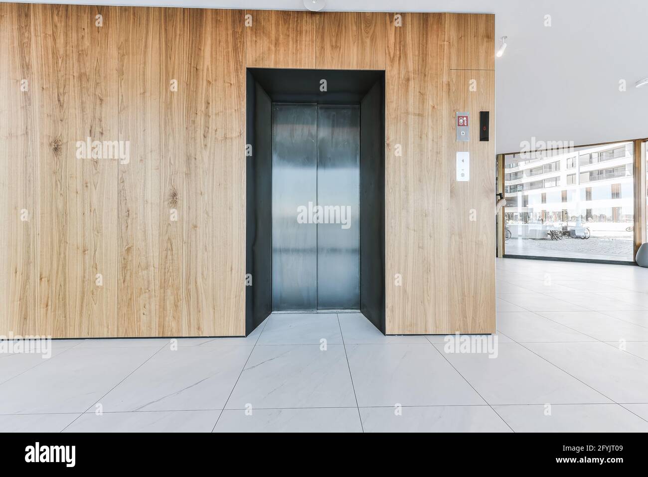 Hall d'entrée de l'immeuble de luxe avec panneaux muraux en bois et ascenseur contre les fenêtres panoramiques Banque D'Images