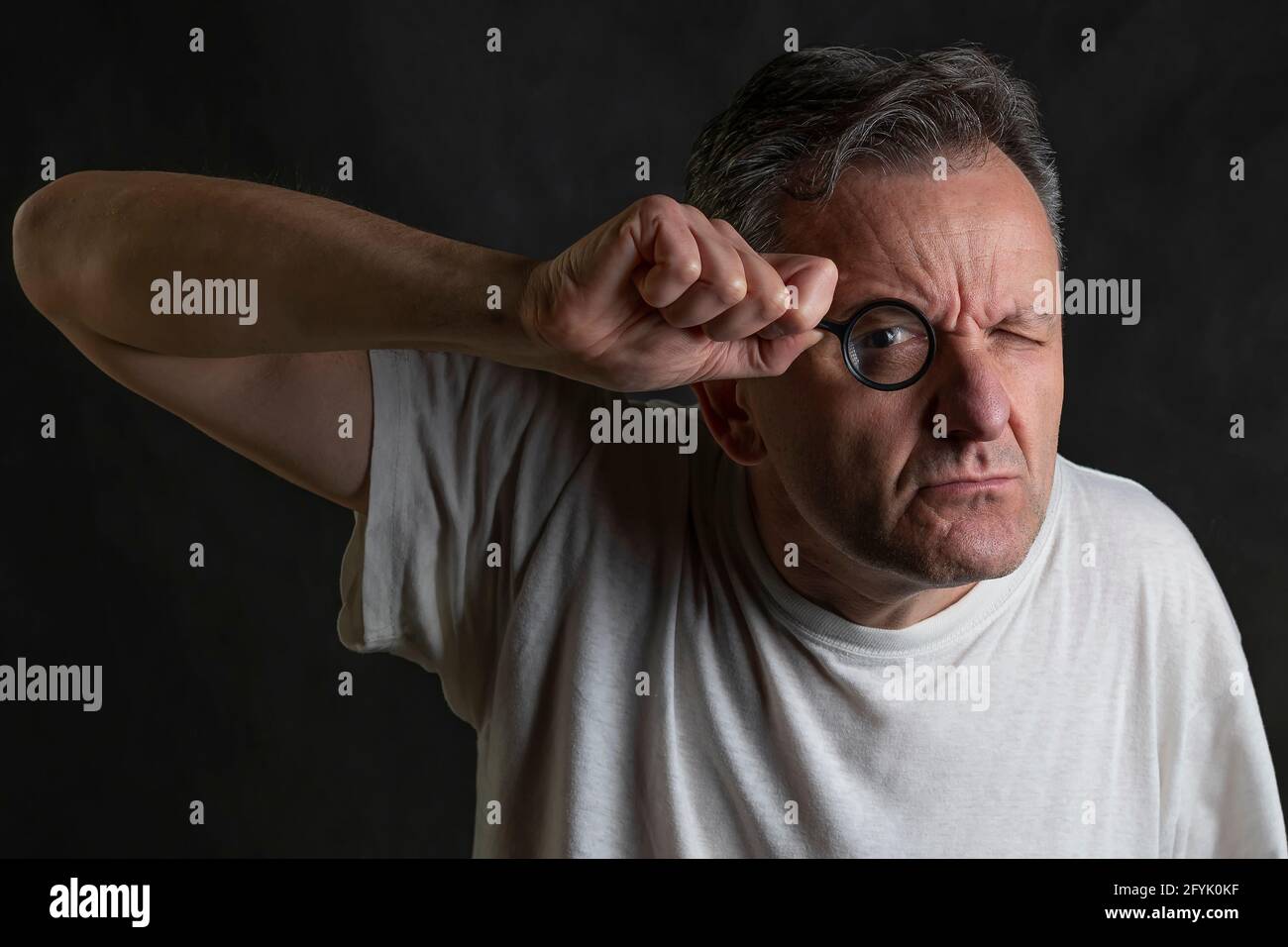 Un homme tient une loupe devant une oeil regardant à travers elle avec une expression très drôle Banque D'Images