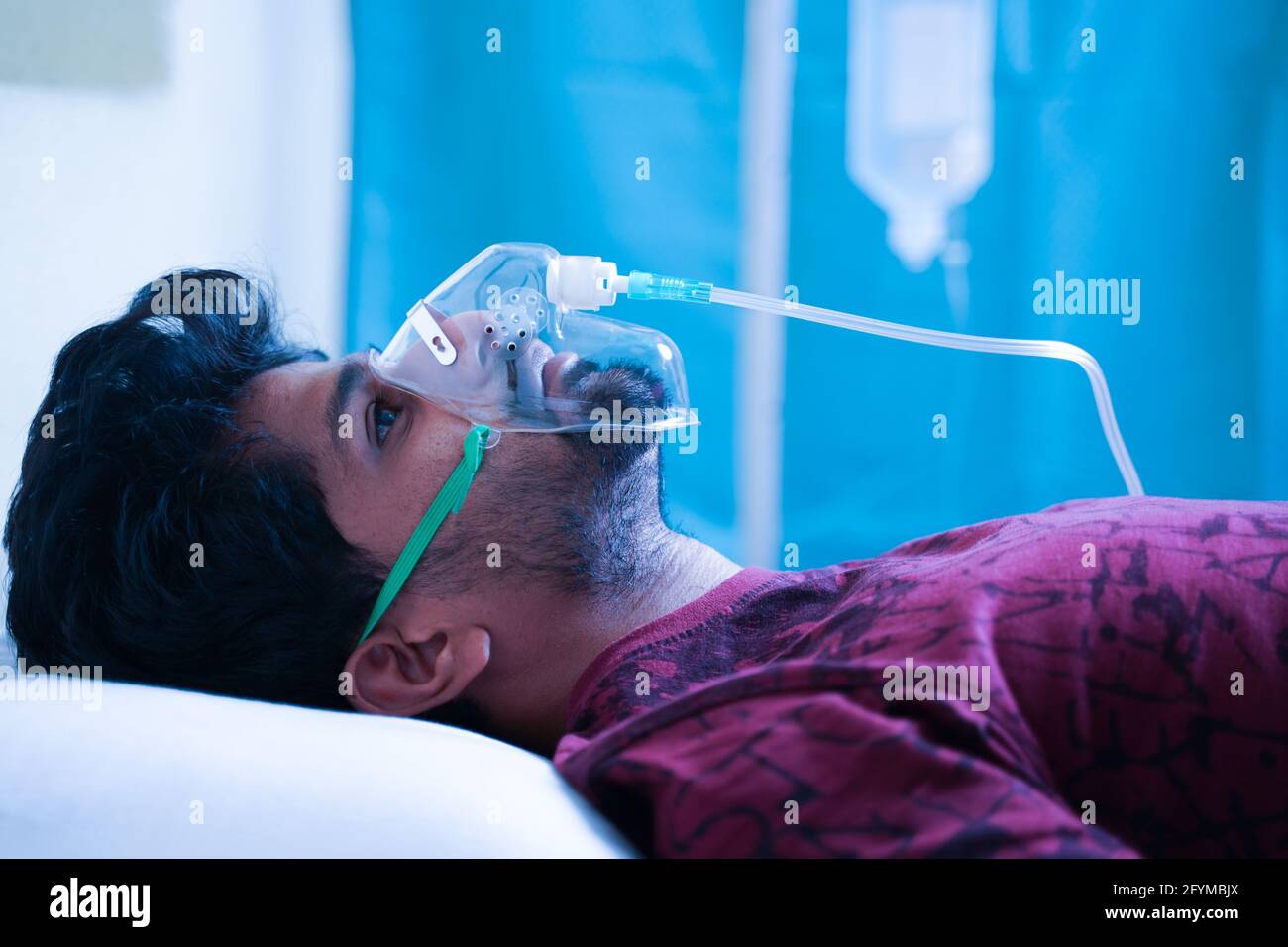 Vue latérale du jeune homme qui respire sur le masque à oxygène du ventilateur À l'hôpital en raison du coronavirus Covid-19 dyspnée ou essoufflement - concept de covid infectant Banque D'Images
