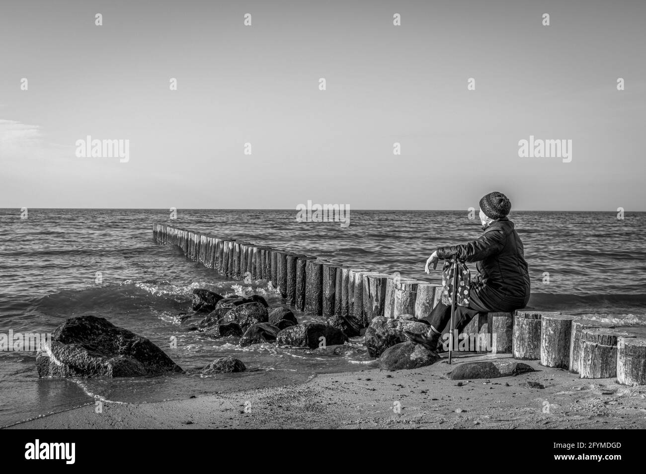 Vieille dame avec une canne assise sur le bord de mer et regardant à l'horizon. Noir et blanc. Banque D'Images
