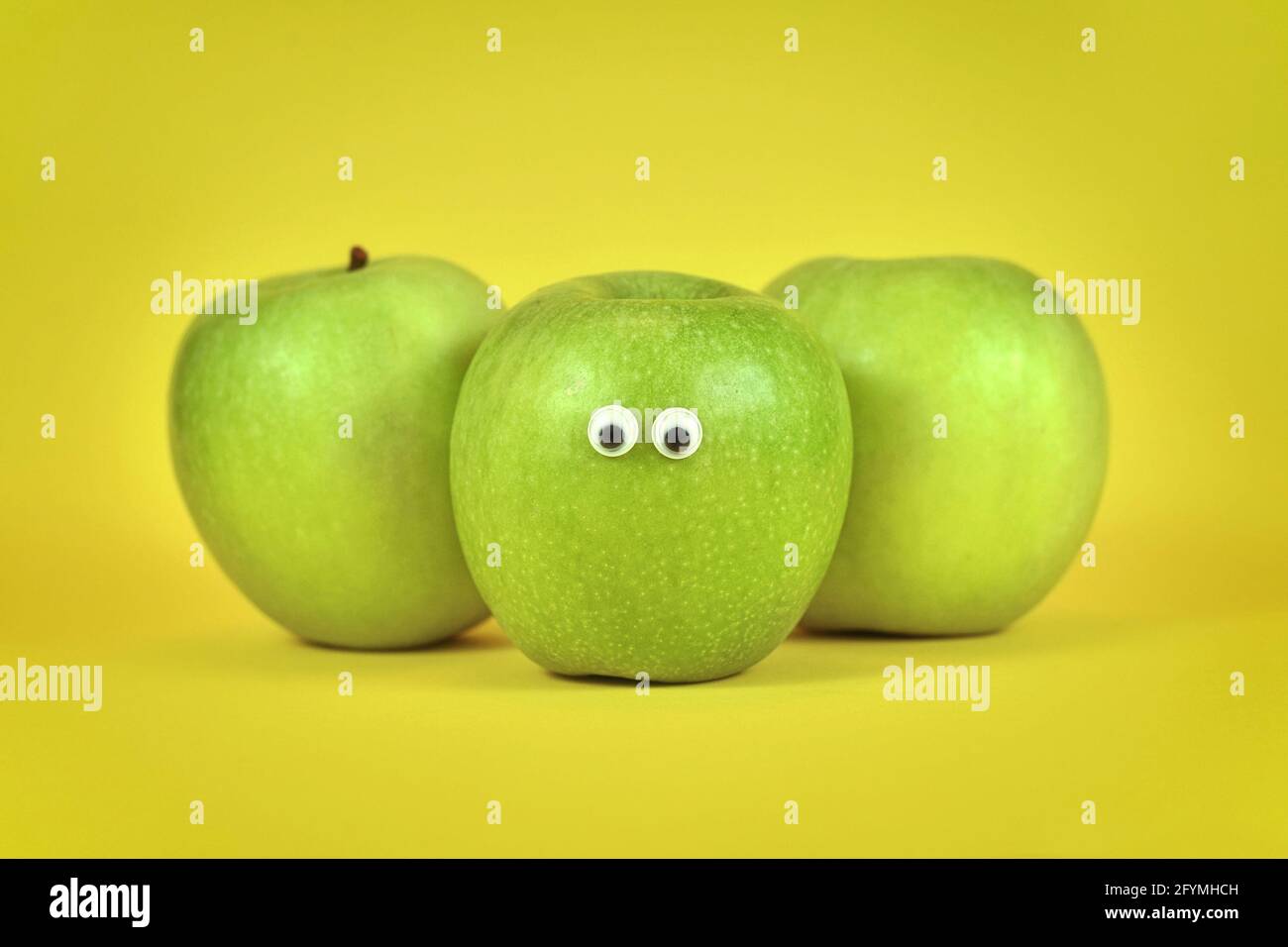 Fruits de pomme verte avec les yeux de googly drôle sur le jaune vif arrière-plan Banque D'Images