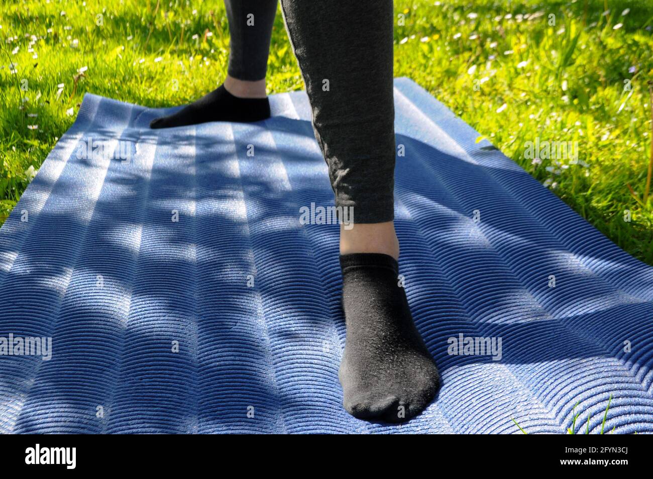 Femme portant des leggings gris et des chaussettes noires, pratiquant le yoga  et se tenant dans le guerrier deux positions sur un tapis bleu sur l'herbe  verte en extérieur Photo Stock -