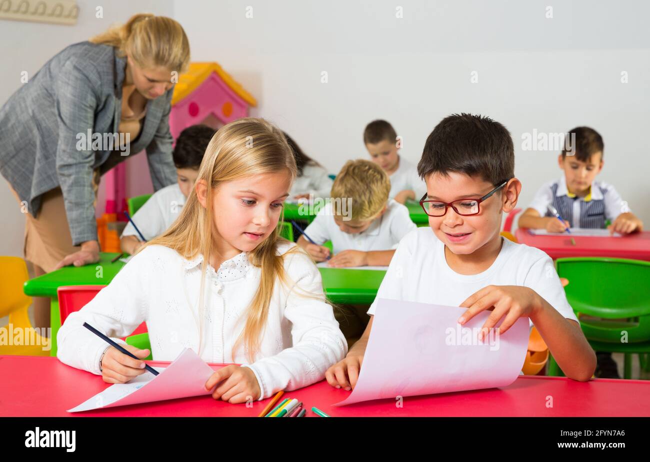 Les élèves heureux assis bavardant à leçon à l'école élémentaire Banque D'Images
