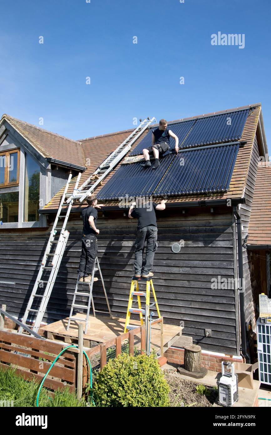 Ingénieur en chauffage installant des tubes de collecte de chaleur solaire sous vide au sud Vue sur le toit de l'Ecohouse dans les Cotswolds au Royaume-Uni Banque D'Images