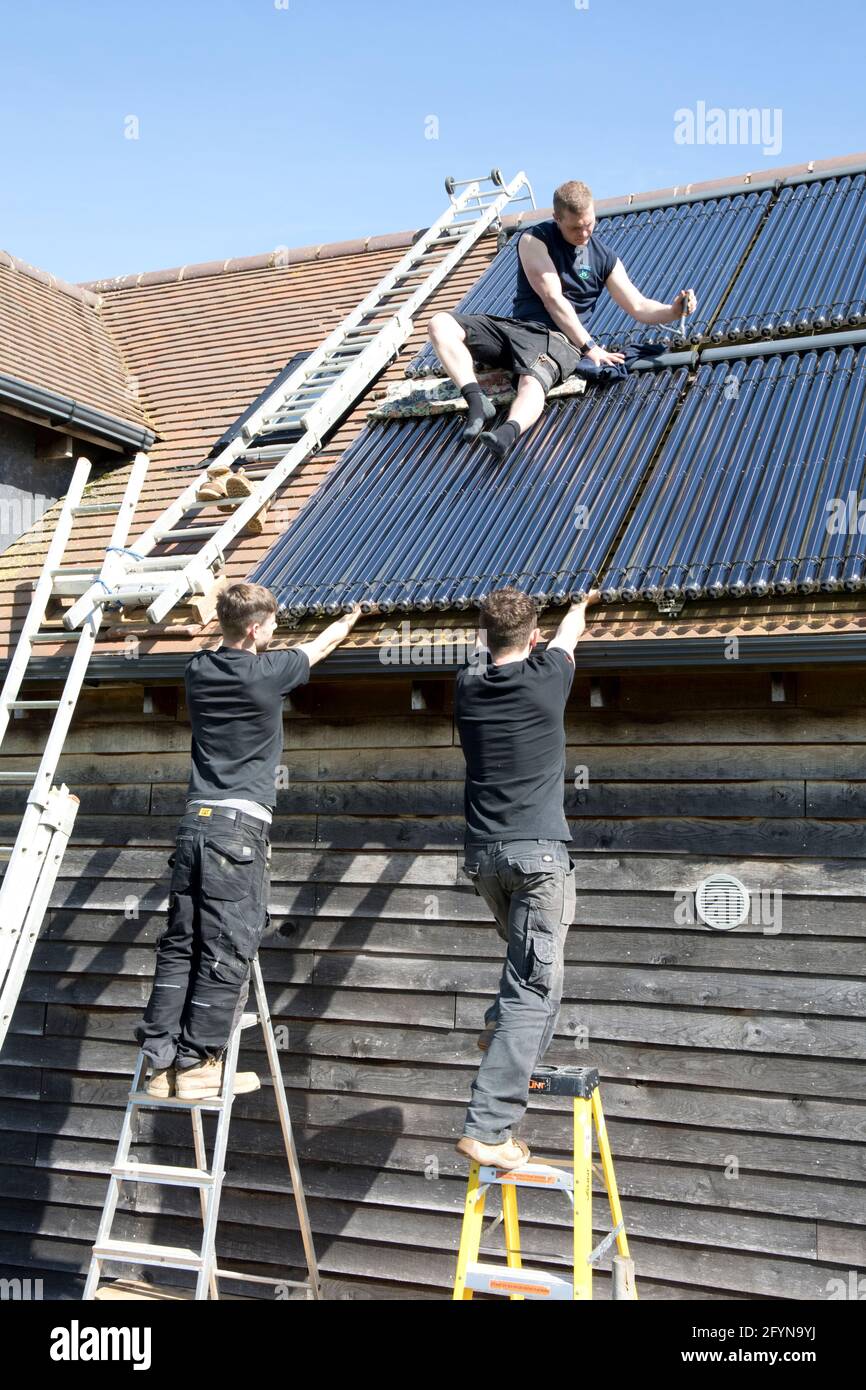 Ingénieur en chauffage installant des tubes de collecte de chaleur solaire sous vide au sud Vue sur le toit de l'Ecohouse dans les Cotswolds au Royaume-Uni Banque D'Images