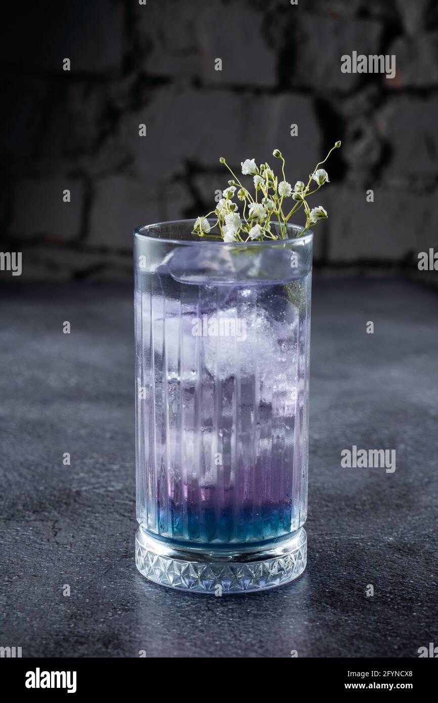 Un cocktail dans un grand verre de liqueur bleue et de glace, décoré de  fleurs blanches sur fond gris Photo Stock - Alamy