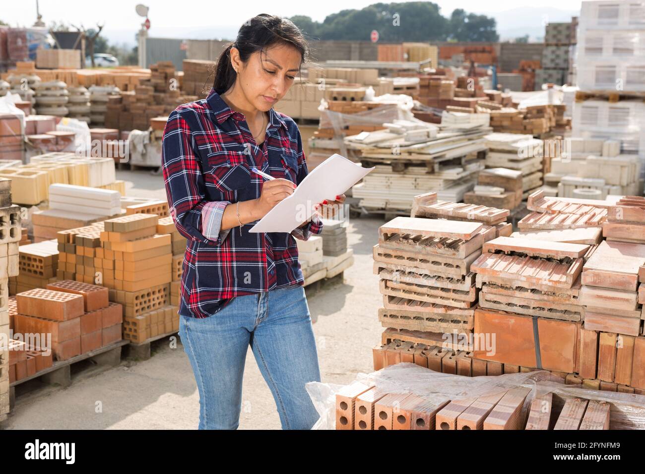 Femme hispanique concentrée travaillant en contrôlant la quantité de briques dans l'entrepôt de matériel Banque D'Images