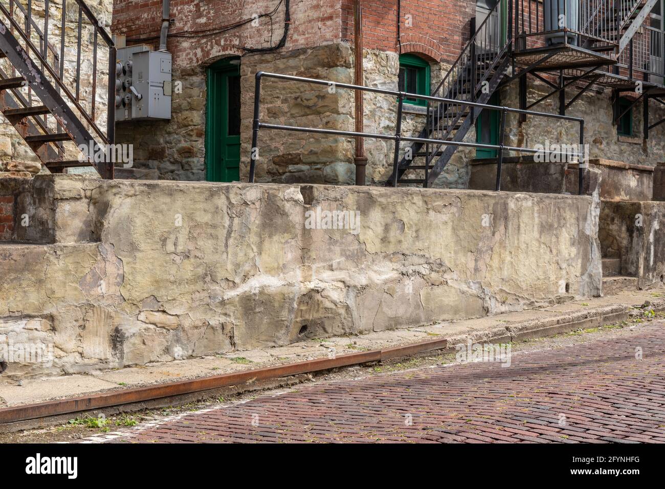 Mur de béton en ruines le long d'une rue en briques rouges, immeuble en briques derrière, aspect horizontal Banque D'Images