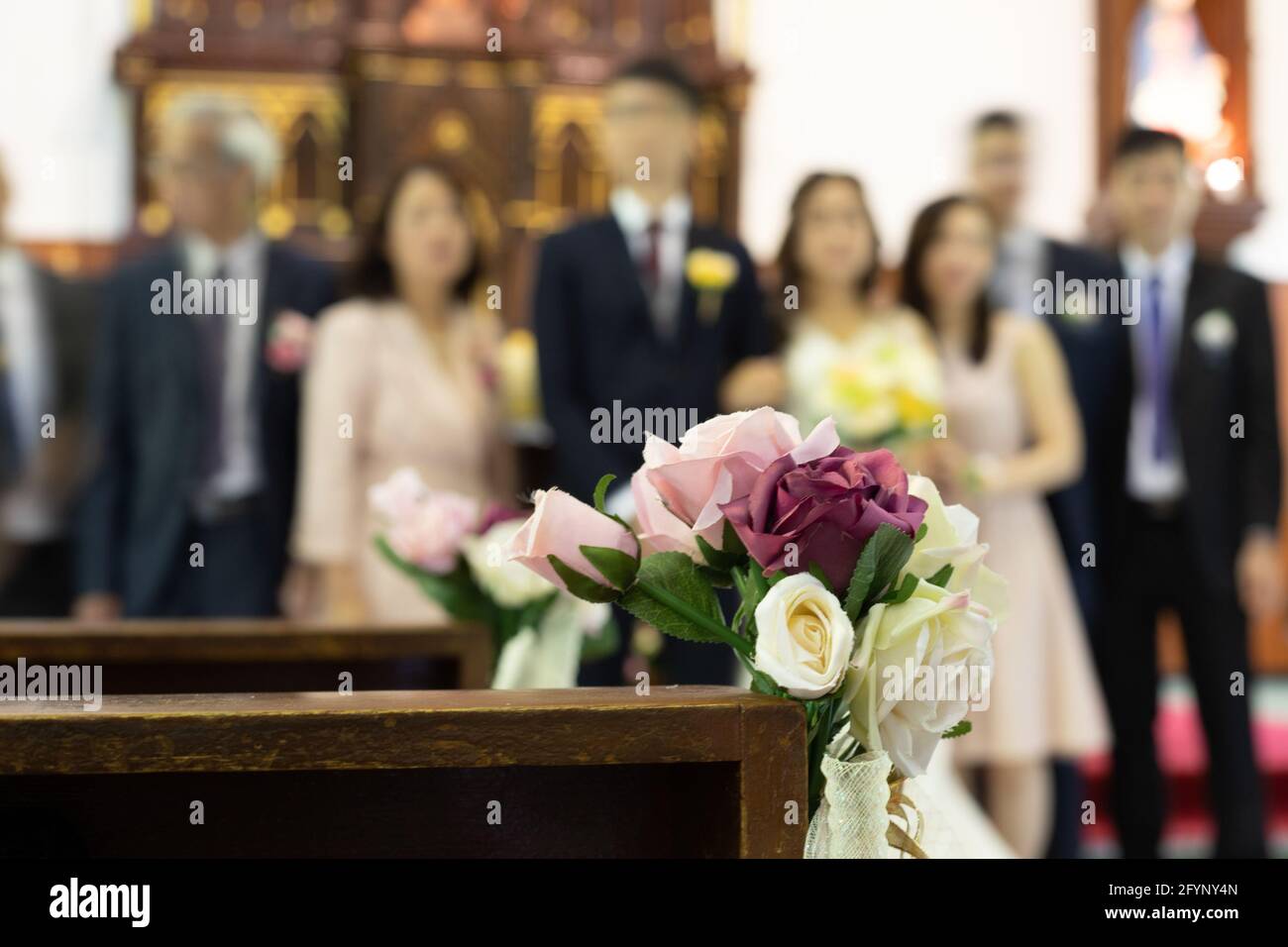 Fleurs roses décoratives avec fond flou de mariée, de marié, d'amis et de parents à l'église lors d'une cérémonie de mariage Banque D'Images
