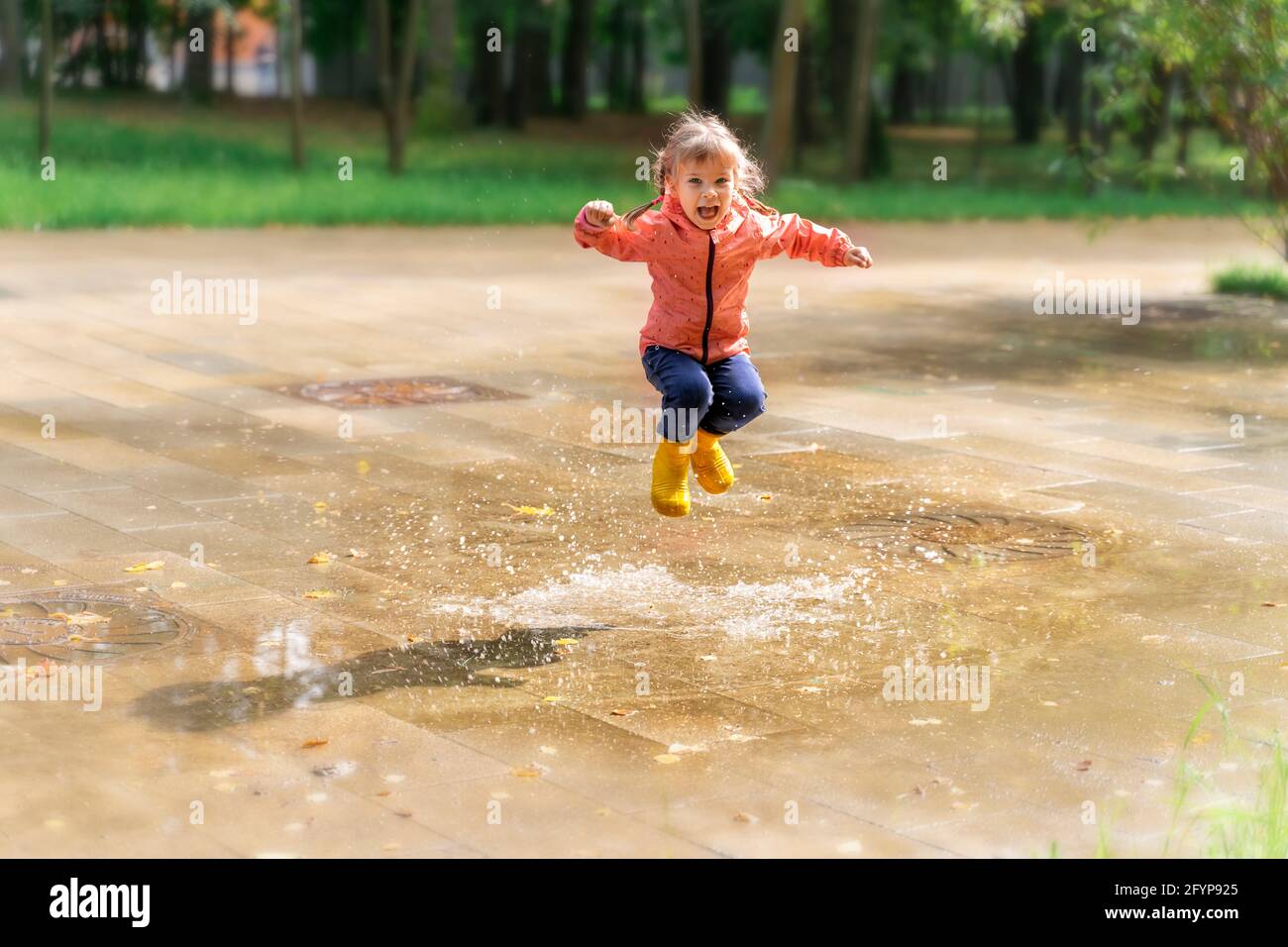bonne fille d'enfant en bottes de pluie a le plaisir de sauter dans les flaques Banque D'Images
