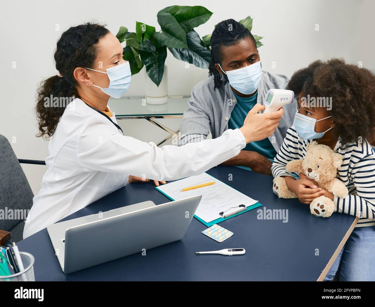 Médecin généraliste vérifiant la température corporelle d'un enfant à  l'aide d'un thermomètre infrarouge. Fille afro-américaine avec son papa  portant une protection Photo Stock - Alamy