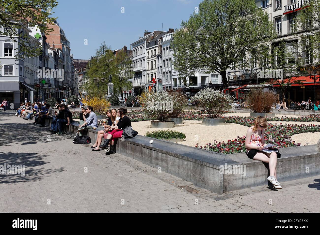 Des touristes sont assis sur un muret place de la cathédrale à Liège Banque D'Images