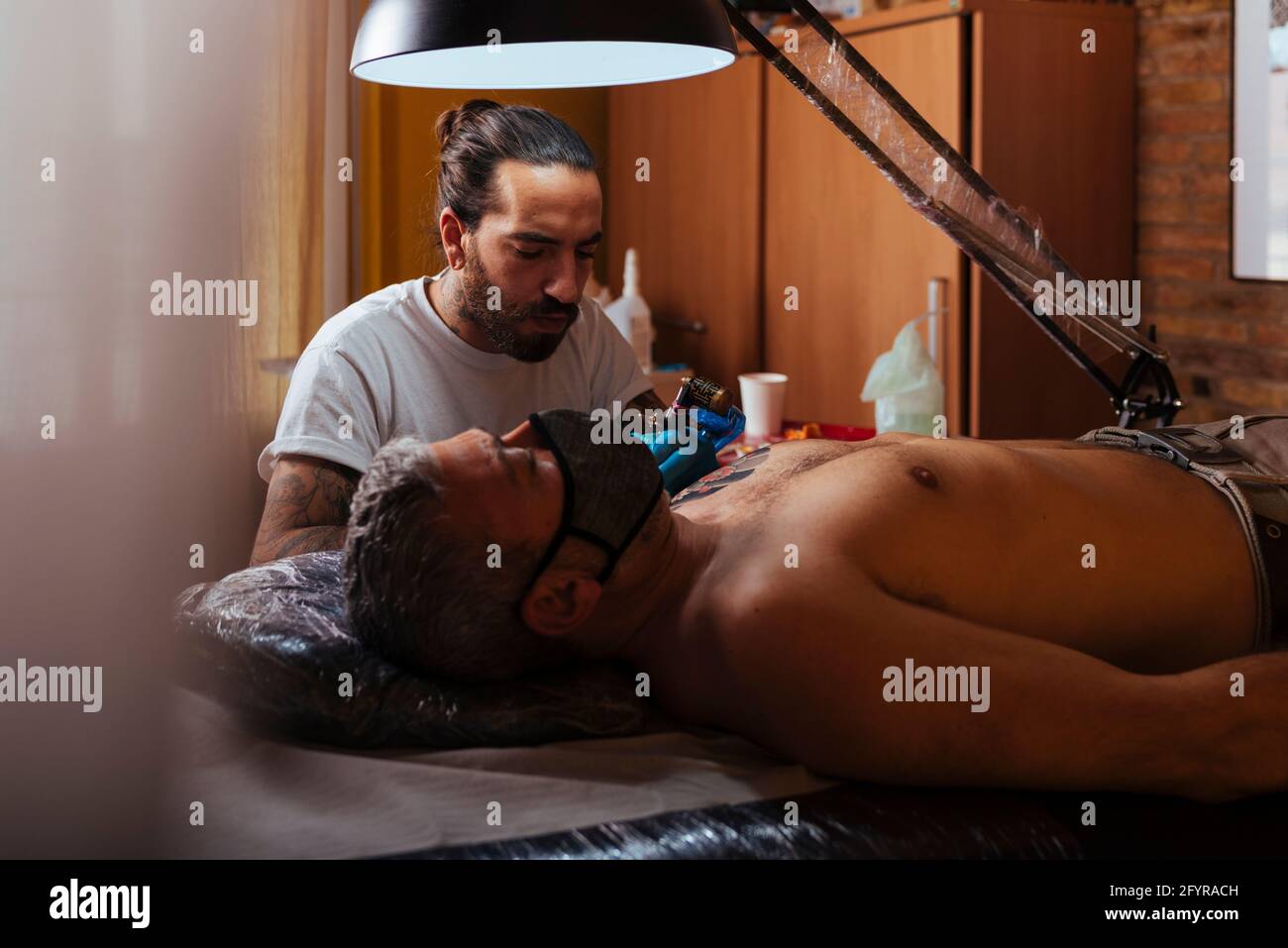 Vue de face d'un tatouage artiste travaillant sur le bras d'un client dans son studio. Banque D'Images