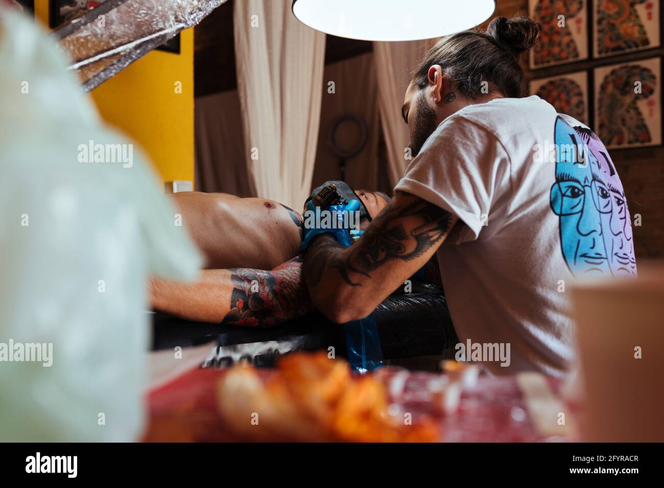 Vue arrière d'un tatouage artiste travaillant sur le bras d'un client dans son studio. Banque D'Images