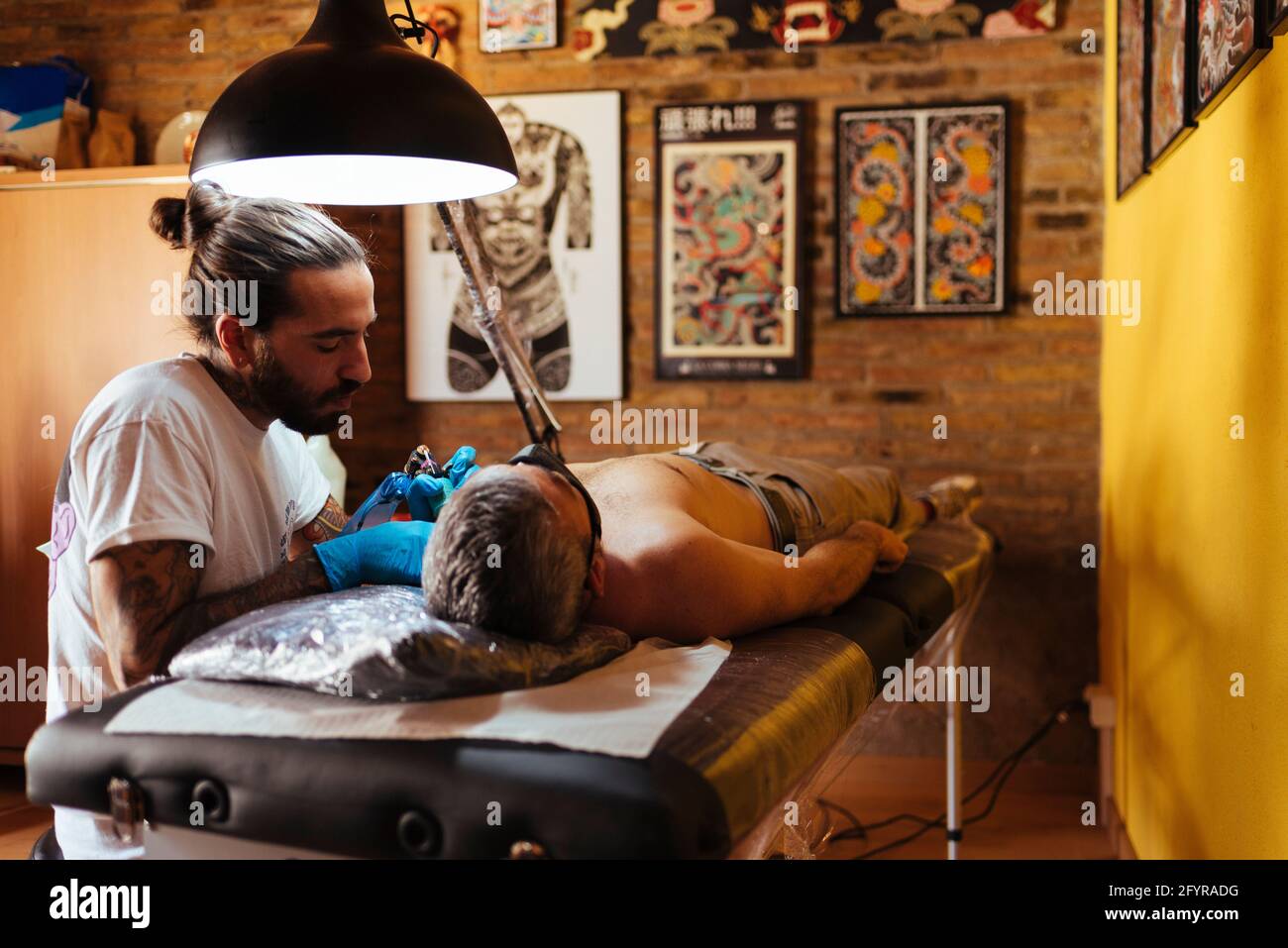 Vue latérale d'un tatouage artiste travaillant sur le bras d'un client dans son studio. Banque D'Images