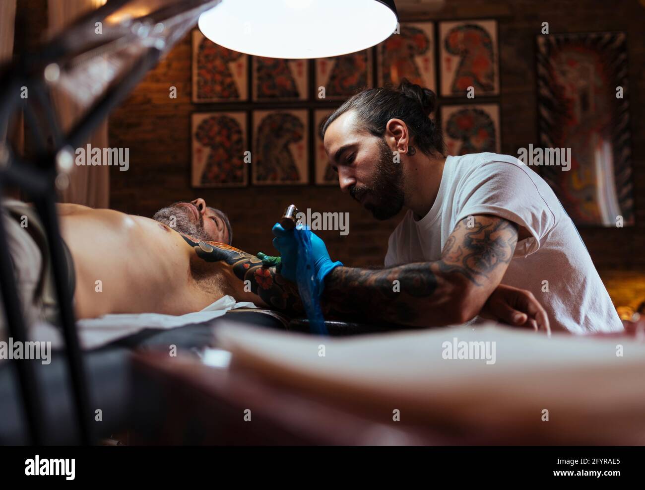Vue latérale d'un tatouage artiste travaillant sur le bras d'un client dans son studio. Banque D'Images
