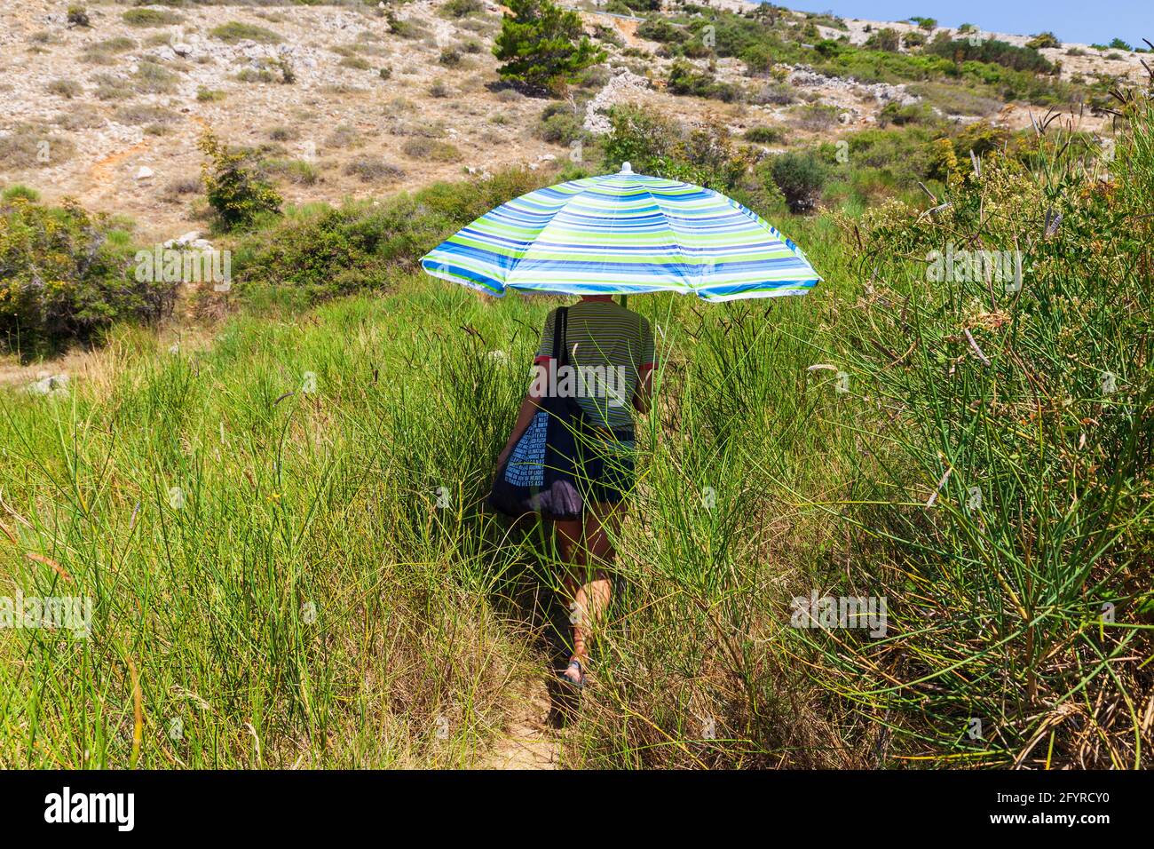 Une femme marche le long de l'herbe de chemin se protégeant elle-même du  soleil avec parasol sur l'île de Krk Photo Stock - Alamy