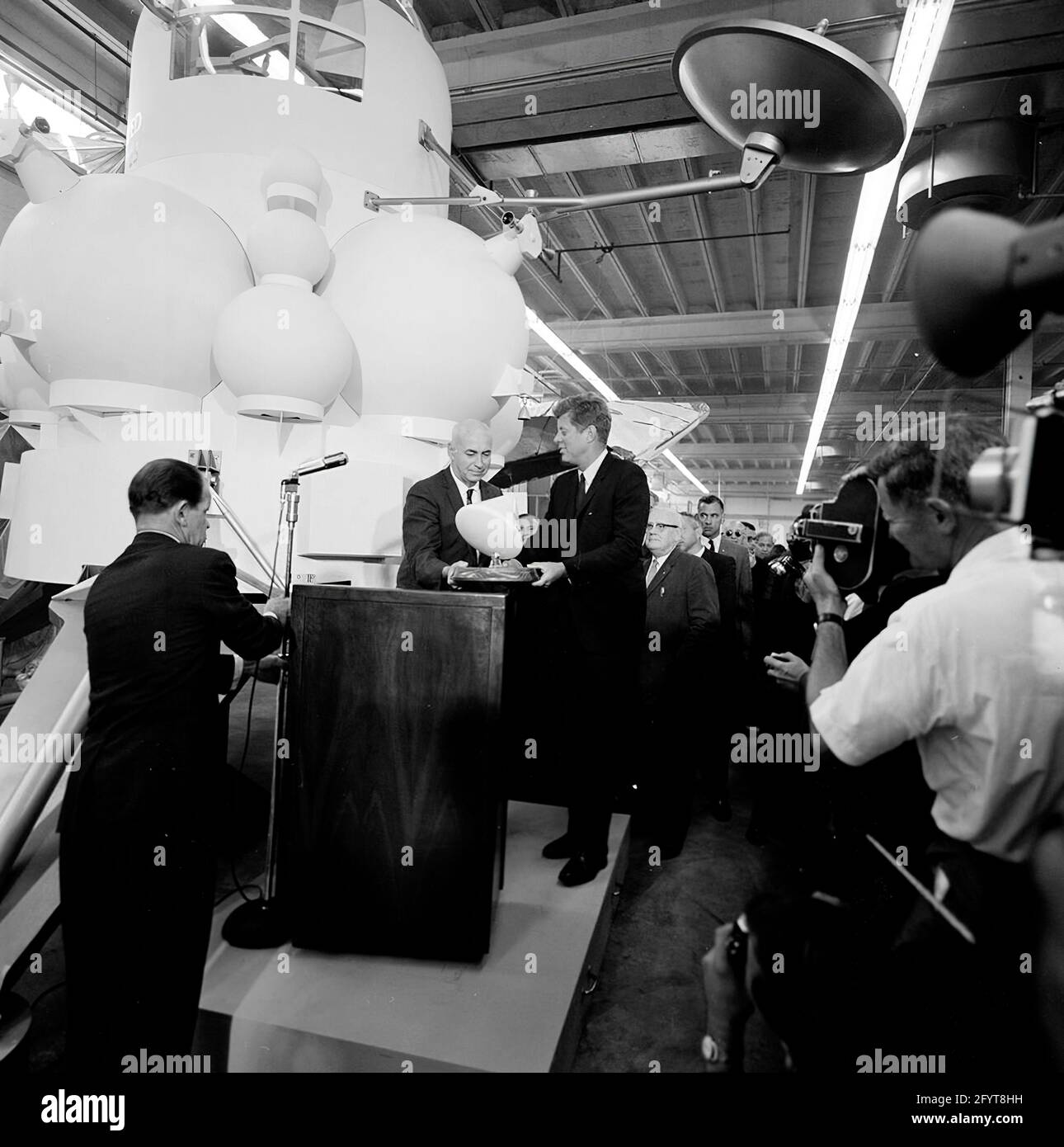 12 septembre 1962le président John F. Kennedy (au lectern) prononce un discours, à la suite d'une visite d'expositions d'engins spatiaux à l'intérieur d'un hangar au Rich Building of the Hided vaisseau spatial Center, Houston, Texas. Le président Kennedy détient un modèle à échelle du module de commande Apollo, qui lui a été présenté par le directeur du centre spatial habité, le Dr Robert Gilruth ; une maquette de l'omble lunaire (également connu sous le nom de « bogue ») est en arrière-plan. En arrière-plan : Administrateur de la National Aeronautics and Space Administration (NASA), Dr. James E. Webb; Gouverneur du Texas, Price Daniel; Banque D'Images