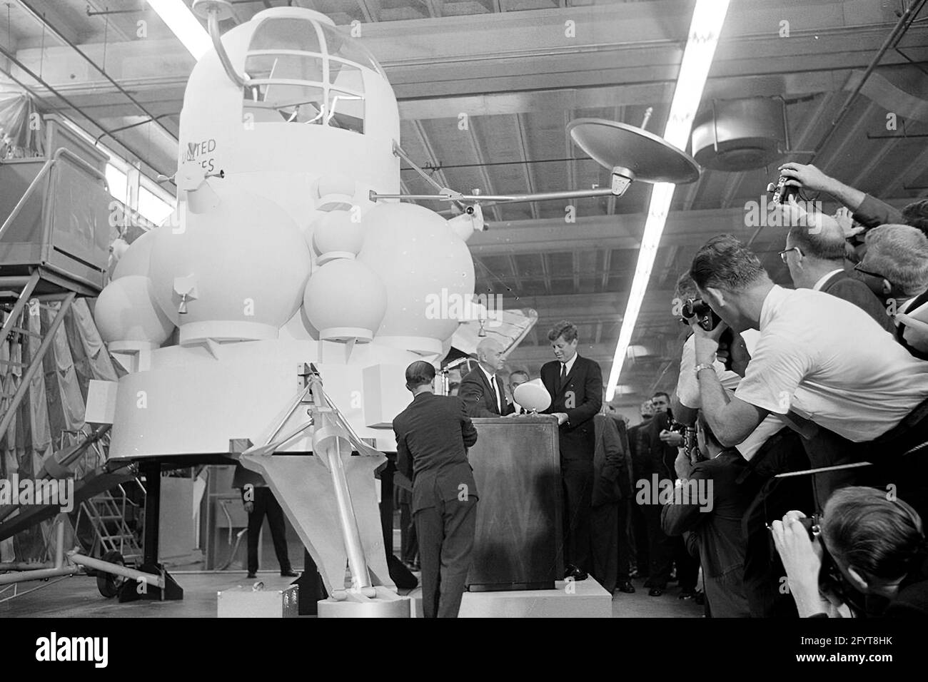12 septembre 1962le président John F. Kennedy (au lectern) prononce un discours, à la suite d'une visite d'expositions d'engins spatiaux à l'intérieur d'un hangar au Rich Building of the Hided vaisseau spatial Center, Houston, Texas. Le président Kennedy détient un modèle à échelle du module de commande Apollo, qui lui a été présenté par le directeur du centre spatial habité, le Dr Robert Gilruth ; une maquette de l'omble lunaire (également connu sous le nom de « bogue ») est en arrière-plan. En arrière-plan : Administrateur de la National Aeronautics and Space Administration (NASA), Dr. James E. Webb; Gouverneur du Texas, Price Daniel; Banque D'Images