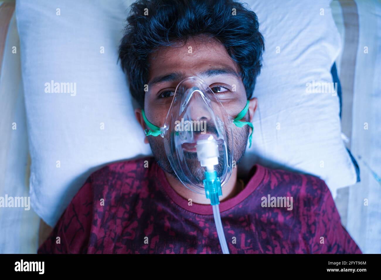Haut de la page vue d'un jeune homme qui respire sur un ventilateur ou un masque à concentrateur d'oxygène à l'hôpital en raison de la dyspnée du coronavirus Covid-19 ou de l'essoufflement - Banque D'Images