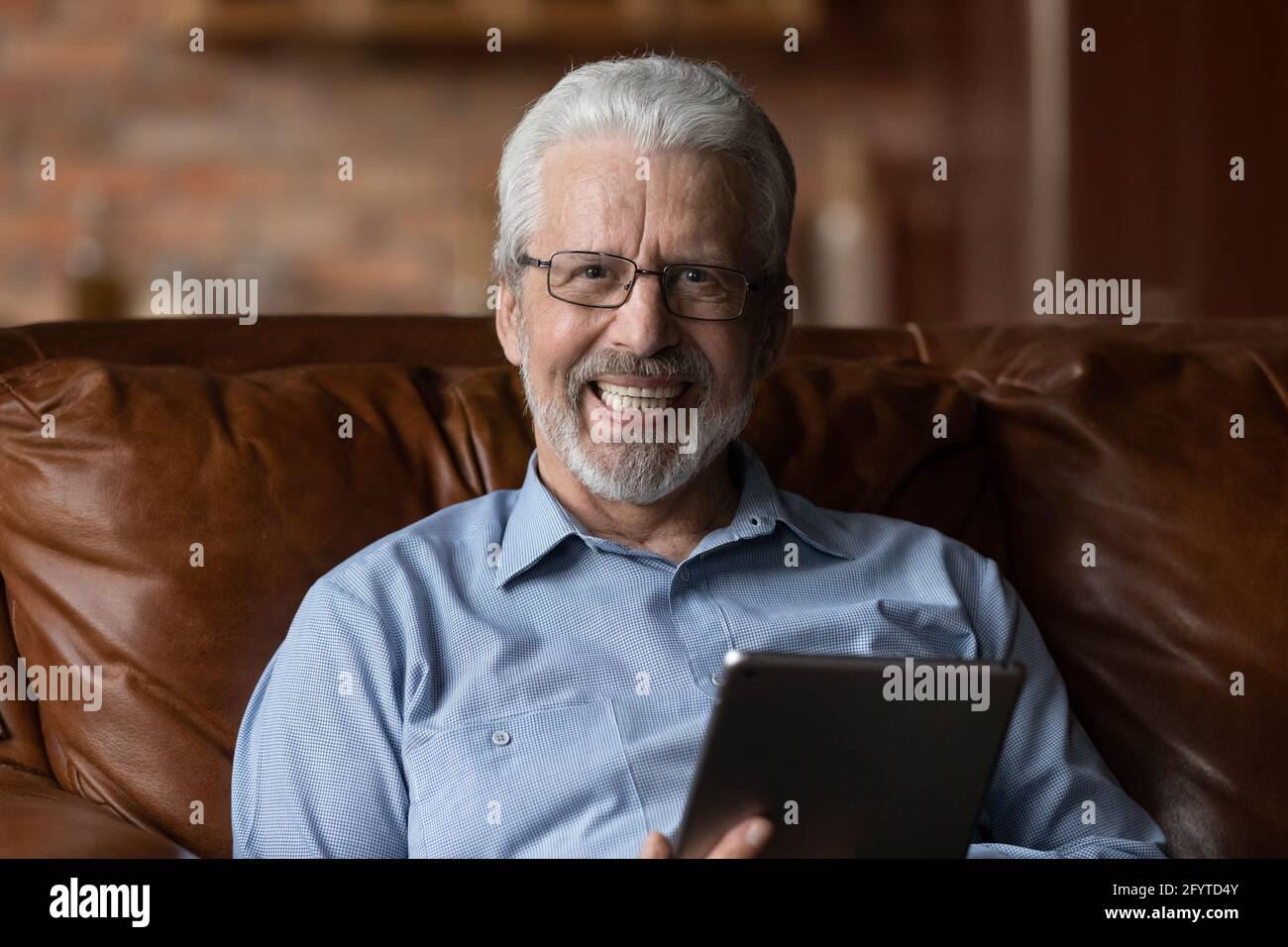 Un homme plus âgé décontracté s'assoit sur un canapé à la maison avec une tablette Banque D'Images
