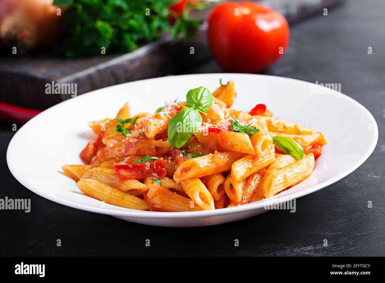 Pâtes italiennes classiques penne alla arrabiata au basilic et au parmesan fraîchement râpé sur une table sombre. Pâtes Penne à la sauce Chili arrabbiata. Banque D'Images