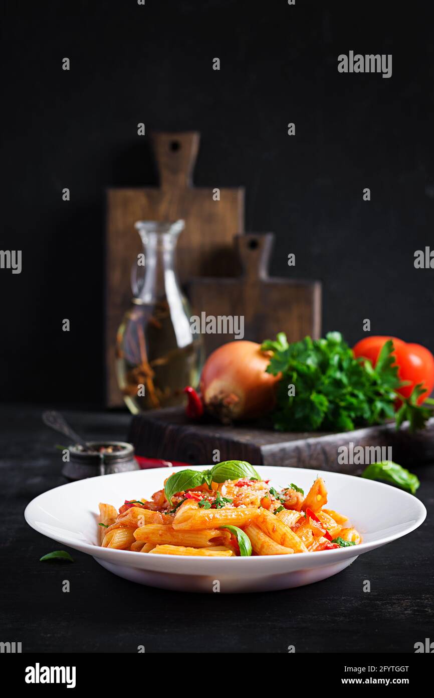 Pâtes italiennes classiques penne alla arrabiata au basilic et au parmesan fraîchement râpé sur une table sombre. Pâtes Penne à la sauce Chili arrabbiata. Banque D'Images