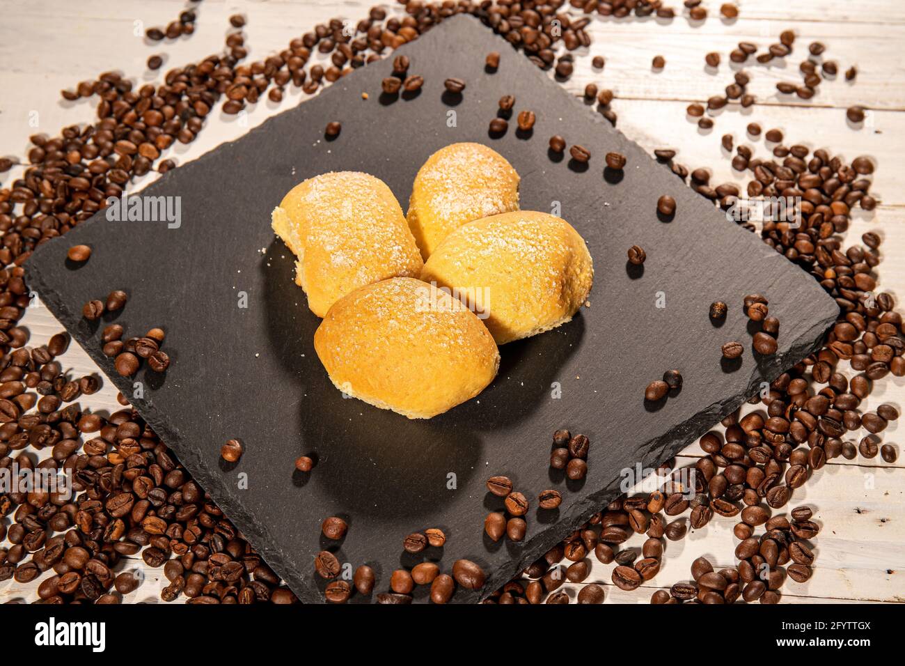 Quatre biscuits faits maison sur une plaque de cuisson entourée de grains de café. Une table en bois blanc sur l'arrière-plan. Banque D'Images