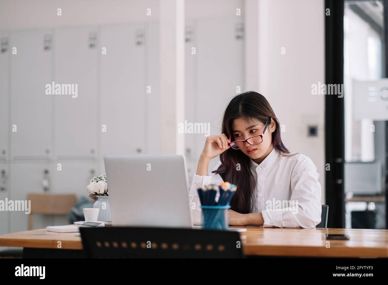 Photo de la belle femme d'affaires asiatique pleine de ressources avec des lunettes regardant sérieusement ordinateur portable regardant la formation en ligne au bureau à domicile. Banque D'Images