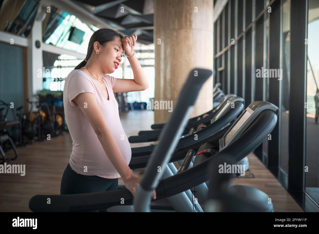 Femme asiatique enceinte fatiguée s'exerçant dans la salle de gym à l'intérieur de la marche sur un tapis roulant pour une forme et un style de vie actif pendant grossesse Banque D'Images