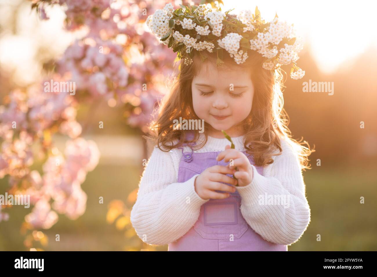 Belle petite fille adorable 2-3 ans portent une couronne de fleurs au  coucher du soleil et fleur de cerisier à l'arrière-plan. Enfance. Saison de  printemps Photo Stock - Alamy