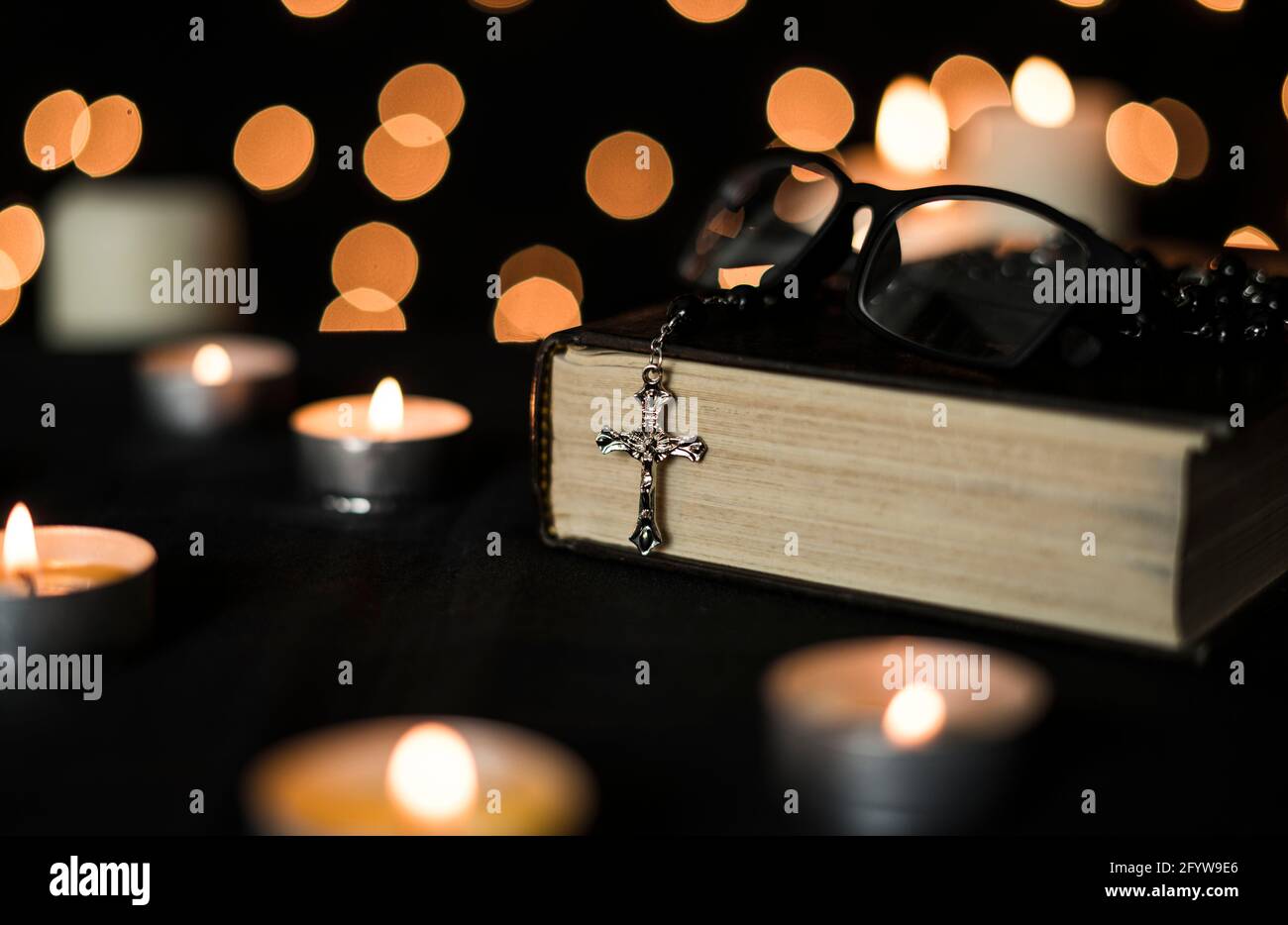 Rosary sur la sainte bible avec des bougies et des lumières de bokeh arrière-plan. Banque D'Images