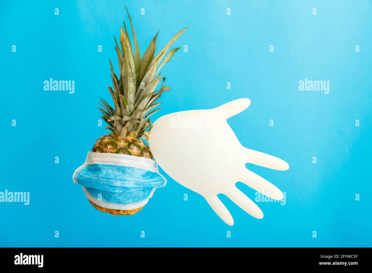 Ananas dans un masque médical avec gant médical en caoutchouc sur fond bleu. Ananas fruits utilisez des produits d'hygiène personnels de soins de santé l'été Banque D'Images