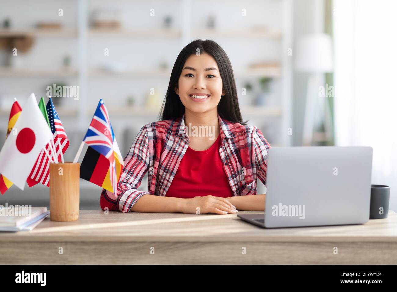 Femme asiatique souriante assise à table avec drapeaux internationaux et Ordinateur portable Banque D'Images