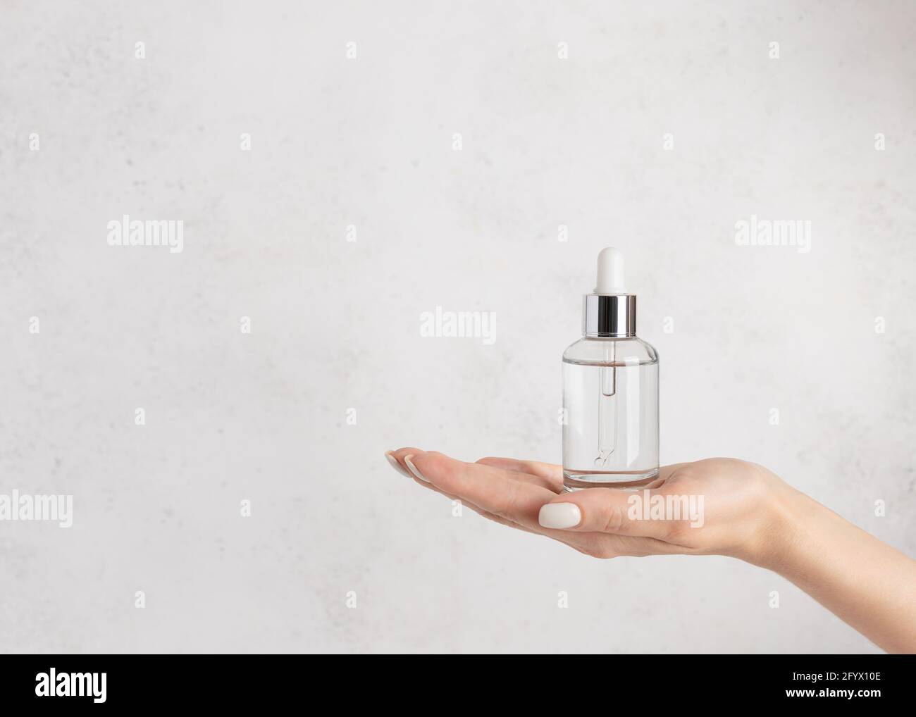main de femme tenant un flacon en verre avec du sérum hydratant. Beauté cosmétique concept de soin de la peau. Fond blanc en béton. Image horizontale Banque D'Images