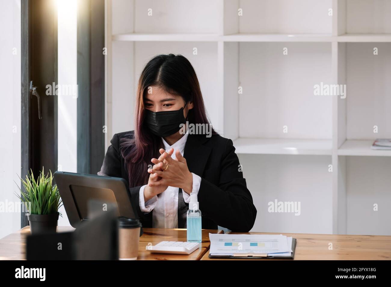 Femme d'affaires avec masque pour communiquer avec son collègue par vidéo Appelez pendant que vous travaillez au bureau pendant la pandémie COVID-19 Banque D'Images