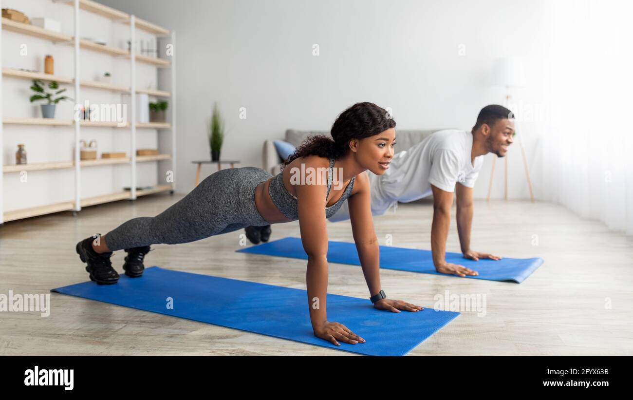 Couple noir millénaire debout en position de planche sur des tapis de yoga à la maison, panorama Banque D'Images