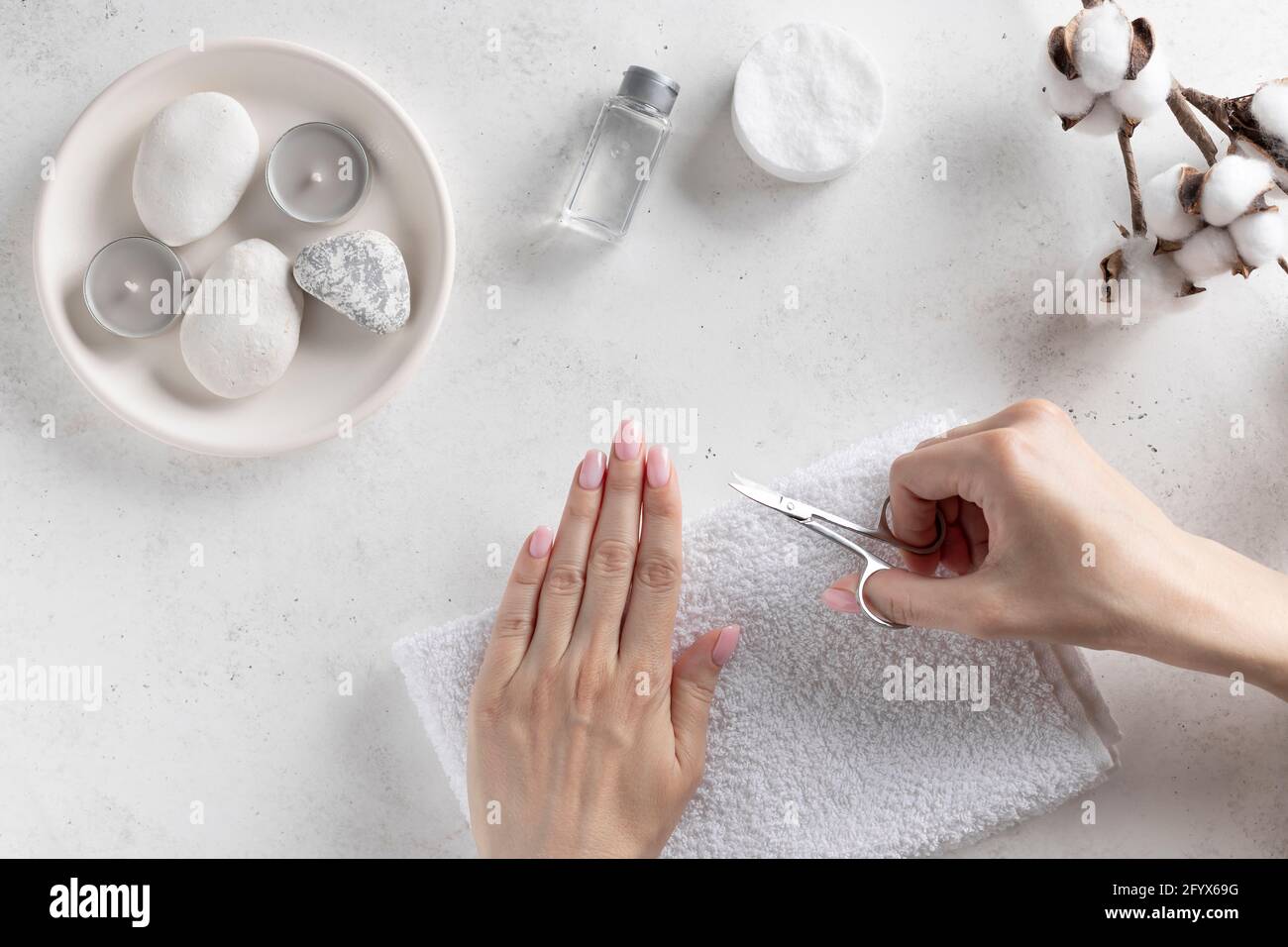 jeune femme coupant des ongles avec des ciseaux de manucure. concept d'hygiène. Arrière-plan blanc avec bougies et fleurs en coton. Vue du dessus. Espace pour les copies Banque D'Images