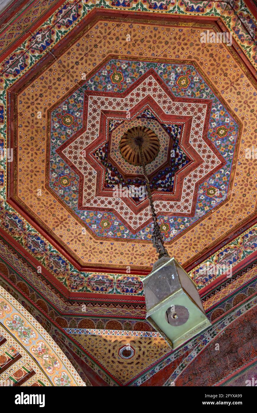 La lampe marocaine ornée est suspendue à un plafond peint en bois de cèdre, également connu sous le nom de Zouak, au Palais Bahia, Marrakech, Maroc, Afrique du Nord. Banque D'Images