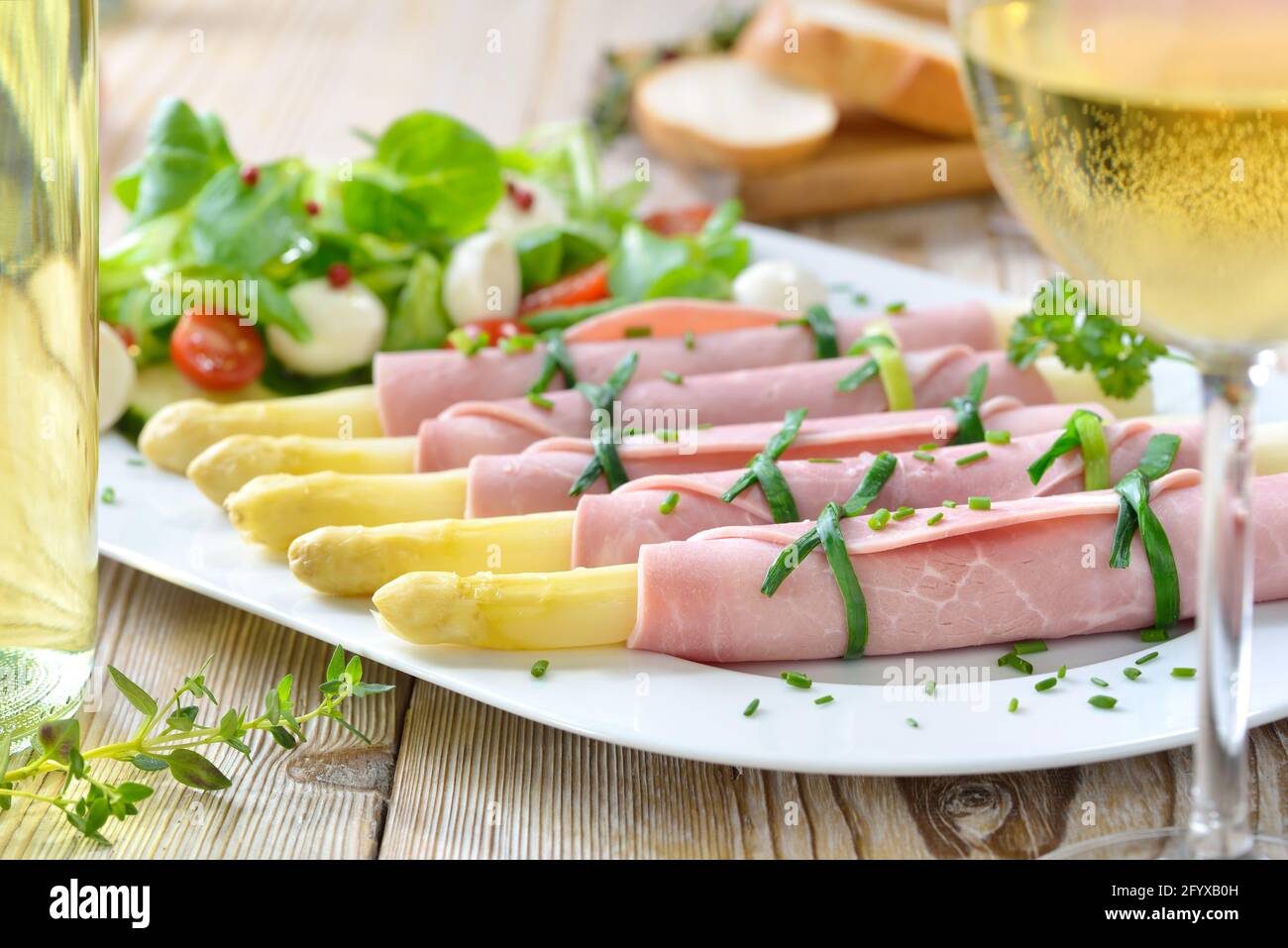 Salade de printemps délicieuse aux asperges, roulé dans du jambon cuit sur un plateau blanc, servi avec un jeune vin blanc sec et des tranches de baguette Banque D'Images