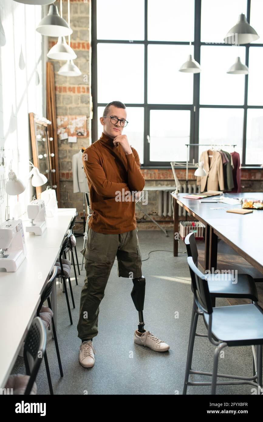 Jeune homme avec prothèse de jambe debout entre les tables dans l'atelier Banque D'Images